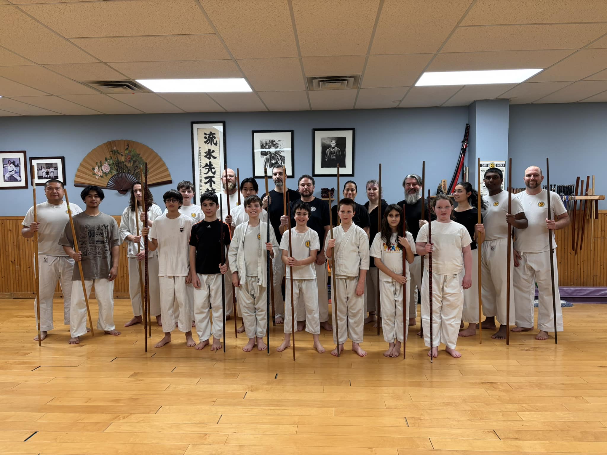 Group photo of students and instructors at Guelph Budokan Centre practicing Okinawan Goju-Ryu karate with bo staffs in a martial arts dojo.